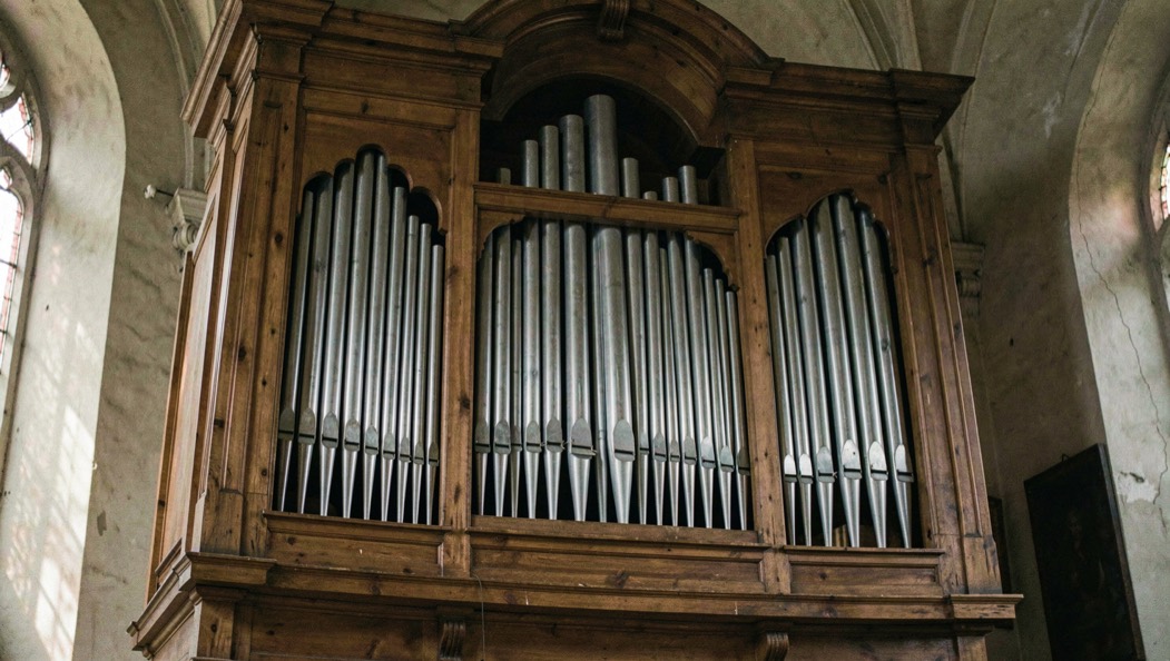 Facciata di un organo storico con canne di stagno allineate per altezza dentro una cornice lignea, penombra di chiesa e luce laterale